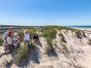 A family on a sandy beach with dunes and a building in the background.