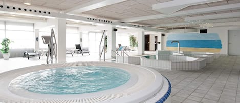 A large indoor swimming pool with a hot tub, lounge chairs, and a mural on the wall.