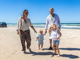 Una familia caminando sobre una playa arenosa con el océano al fondo.