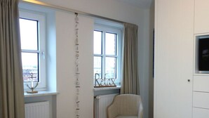 A room with a bed, a chair, and two windows with curtains. - Holiday Apartment Lust on Sylt (Sylt)