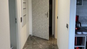 A hallway with a marble floor, a white door, and a kitchen area with a red kettle. - Holiday Apartment Siuerlanner (Sundern)