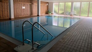 An indoor swimming pool with wooden panel walls, clear glass windows, and tiled flooring. - Holiday Apartment Siuerlanner (Sundern)