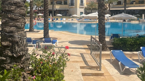 A poolside area with lounge chairs, palm trees, and a building with a tiled roof. - Belvilla by OYO Mar Menor (Torre-Pacheco)