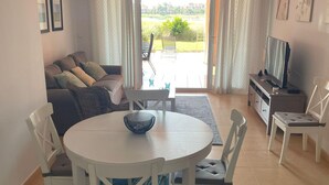 A living room with a sofa, a dining table with chairs, a TV stand, and a view of the outdoors. - Belvilla by OYO Mar Menor (Torre-Pacheco)