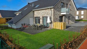A modern house with a sloped roof, a stone facade, and a patio area with a table and chairs. - Holiday Home sea Breeze (Butjadingen)