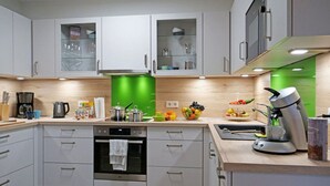 A modern kitchen with white cabinets, a green accent wall, and various appliances including a coffee maker and a kettle. - Holiday Home sea Breeze (Butjadingen)