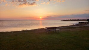 A sunset over a calm body of water with a picnic table and grassy area. - 4 Person Holiday Home in Hemmet (Hemmet)
