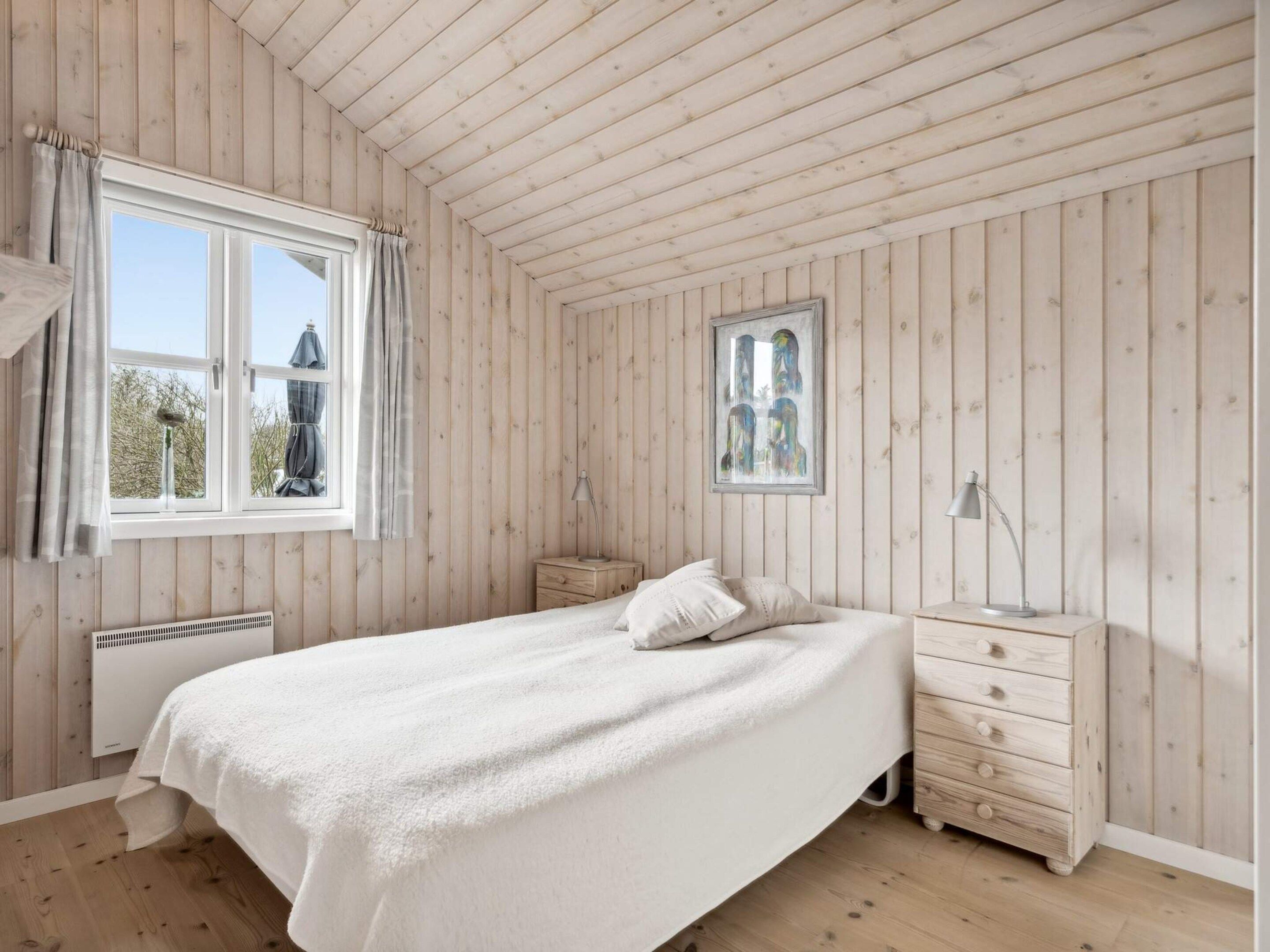 Ein Schlafzimmer mit einem großen Bett, einem Nachttisch, einem Fenster mit Vorhängen und einem gerahmten Bild an der Wand.