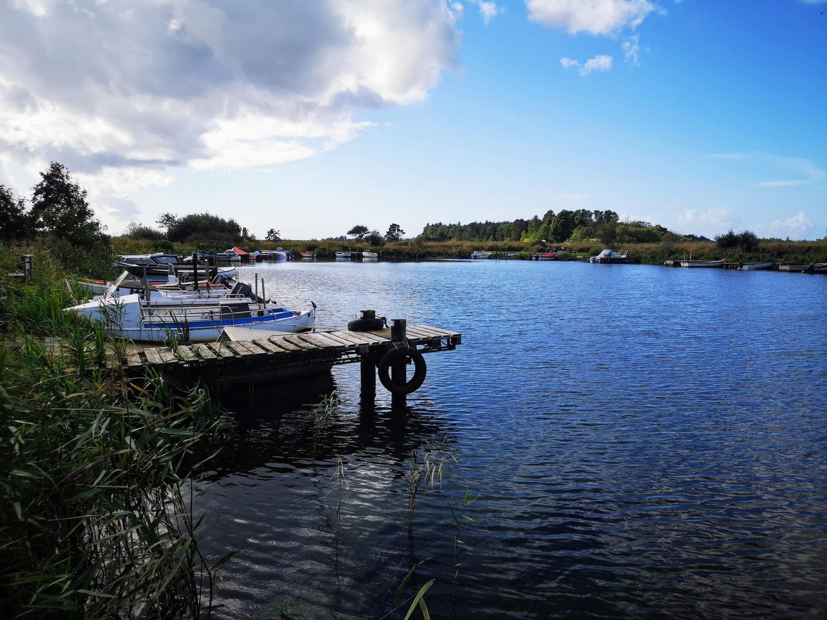 A calm river with boats docked at a wooden pier.