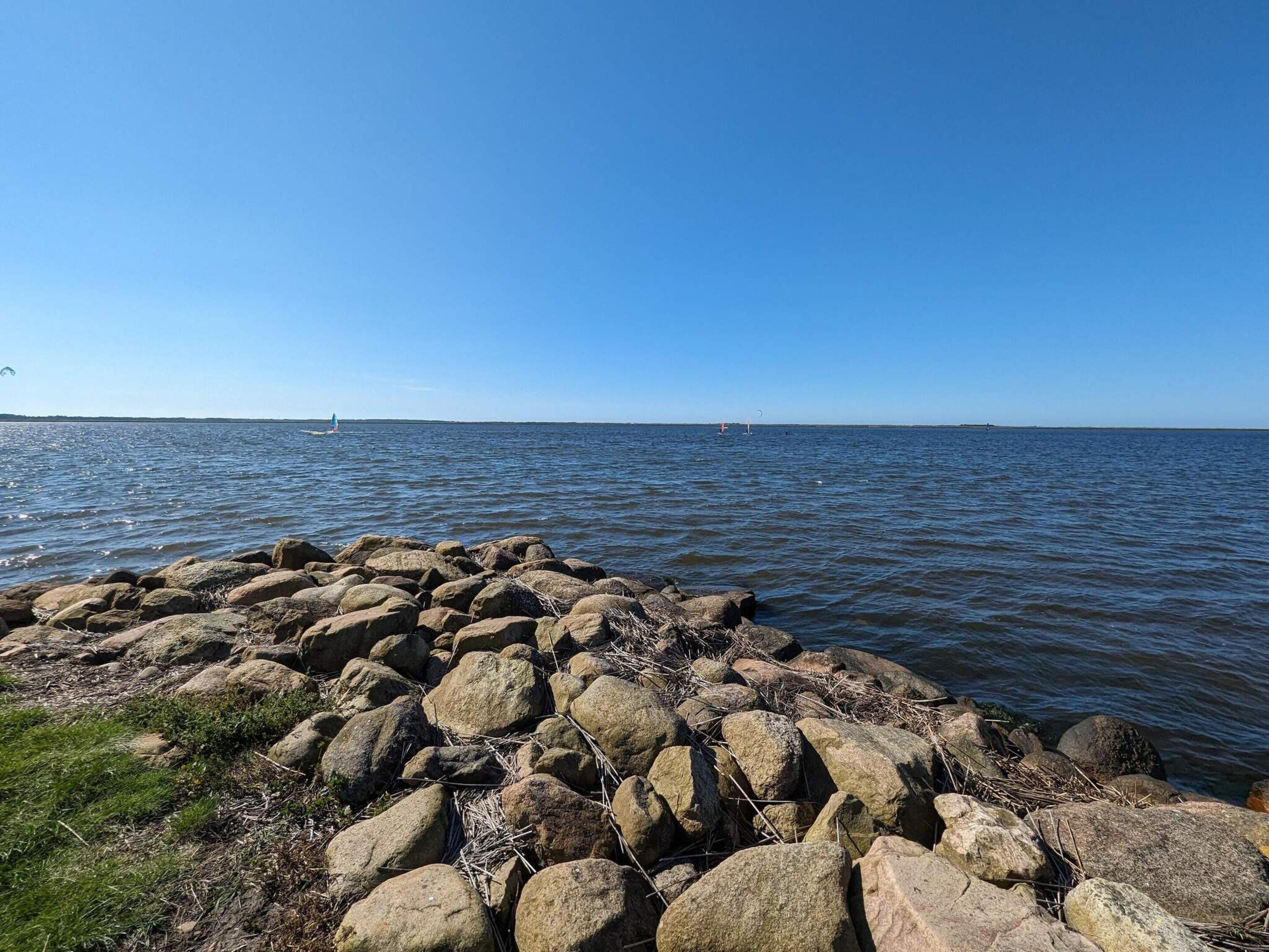 A rocky shoreline with calm water and a clear sky.