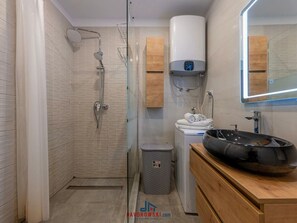 A modern bathroom with a glass shower enclosure, a white toilet, a sink with a black basin, and wooden cabinets. - Donatella -apt 2- met Zeezicht (Medulin)