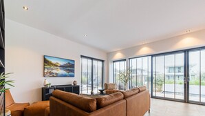 A modern living room with a large brown leather sofa, a black entertainment unit, and a large window with blinds. - Villa in Zeewolde Near Town Center (Zeewolde)