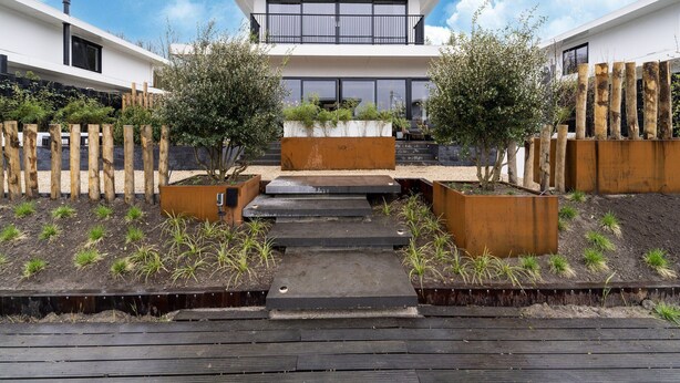 A modern house with a flat roof, large windows, and a wooden fence. There are steps leading to the entrance, and the ground is covered with gravel and plants. - Villa in Zeewolde Near Town Center (Zeewolde)