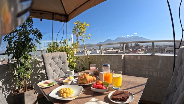A dining table with breakfast items, a view of a cityscape and mountains, and a potted plant. - TERRAMISTICA CENTRO BY CASA CONSUELO   (Arequipa)
