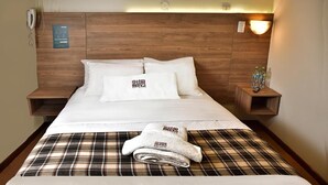 A neatly made bed with white linens and a plaid blanket, a wooden headboard, a bedside phone, and a nightstand with bottled water. - TERRAMISTICA CENTRO BY CASA CONSUELO   (Arequipa)