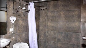 A bathroom with a white toilet, a sink, a shower with a white curtain, and a towel rack. - TERRAMISTICA CENTRO BY CASA CONSUELO   (Arequipa)