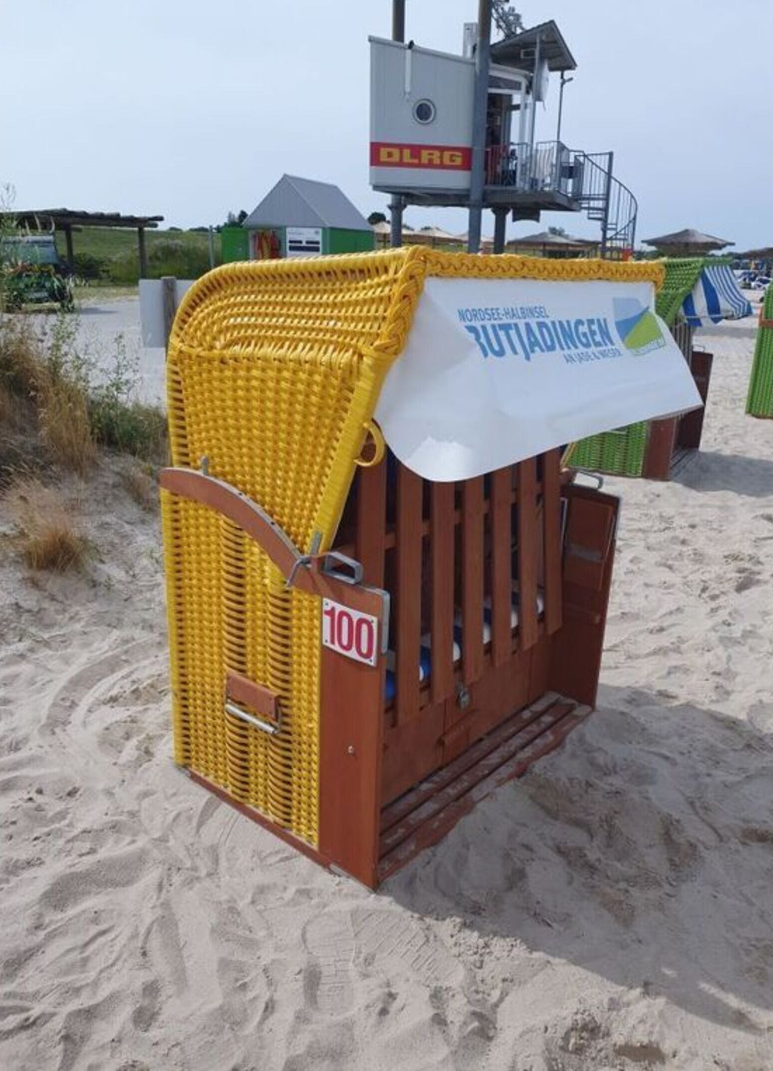 A beachside lifeguard station with a yellow lifeguard chair and a white sign indicating a lifeguard station.