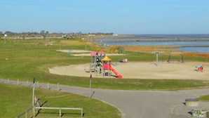 A playground with a slide and climbing structures, surrounded by a sandy area and a grassy field. - Holiday Home Tim Paul (Butjadingen)