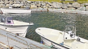 Una marina con diverse imbarcazioni ormeggiate, una costa rocciosa e un veicolo bianco sullo sfondo.