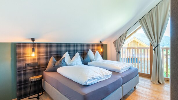 A modern bedroom with a large bed, a small stool, and a view of a wooden deck and mountains. - Chalet in Wolting With Natural Swimming Pond (Tamsweg)