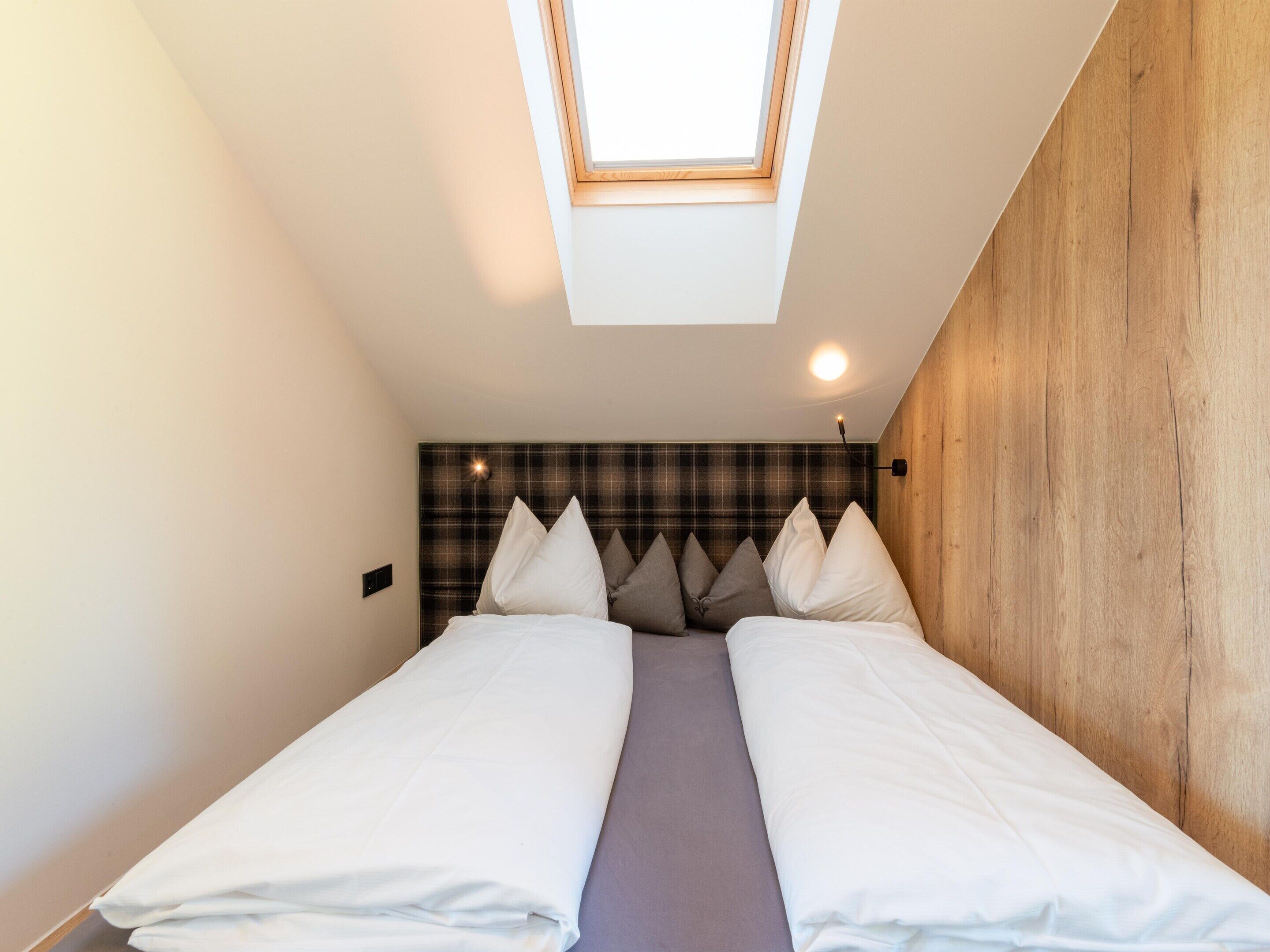 A bedroom with a skylight, a bed with white bedding, a plaid headboard, and a wooden wall.