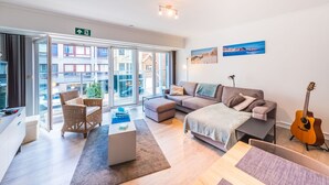 A modern living room with a sofa, a coffee table, a guitar, and a view of the outside. - Studio With Sleeping Area for Family (Middelkerke)