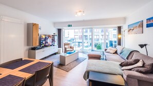 A modern living room with a dining area, a sofa, a coffee table, and a TV. - Studio With Sleeping Area for Family (Middelkerke)