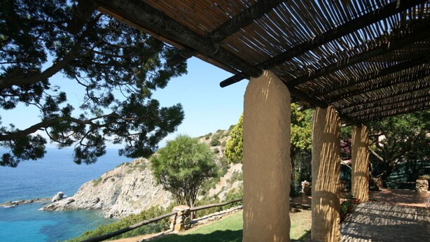 Un área costera con un camino de piedra que lleva a una pérgola de madera con vistas al mar.