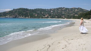 Una playa con una mujer de vestido blanco caminando por la orilla.
