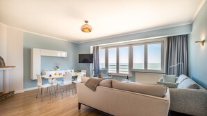 Un salon moderne comprenant un canapé, une table à manger avec des chaises, un téléviseur et une grande fenêtre avec des rideaux.