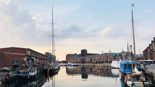 A marina with boats docked, buildings in the background, and calm water reflecting the scene.