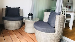 A balcony with wicker furniture, including two chairs and a small table, and a pair of binoculars on the table.