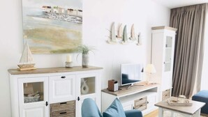 A living room with a blue sofa, a TV, a white cabinet, and a painting on the wall.