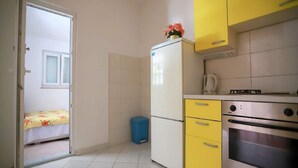 A compact kitchen with yellow cabinets, a white refrigerator, a blue trash bin, and a stove. - Apartments Pezo - Superior Two Bedroom Apartment With Balcony (Baska Voda)