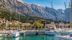 A marina with boats docked, surrounded by mountainous terrain and residential buildings. - Apartments Pezo - Superior Two Bedroom Apartment With Balcony (Baska Voda)