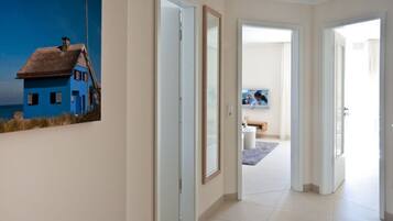 A hallway with a painting of a house by the sea, a television, and a bathroom with a toilet and sink.