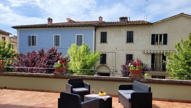 A rooftop terrace with outdoor furniture, a view of a building with multiple windows, and potted plants. - Apartment sleeps 6 located in in the heart  Asciano, with terrace. (Asciano)