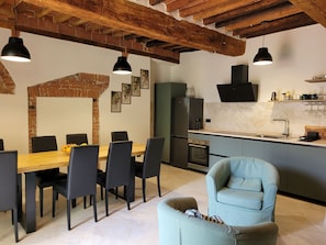 Una cocina moderna con horno empotrado, refrigerador y lavaplatos. Hay una zona de comedor con mesa y sillas de madera.
