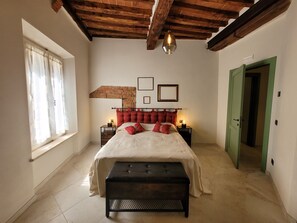 Une chambre à coucher avec un lit, un banc, une fenêtre avec des rideaux, un plafond en bois et une porte verte.