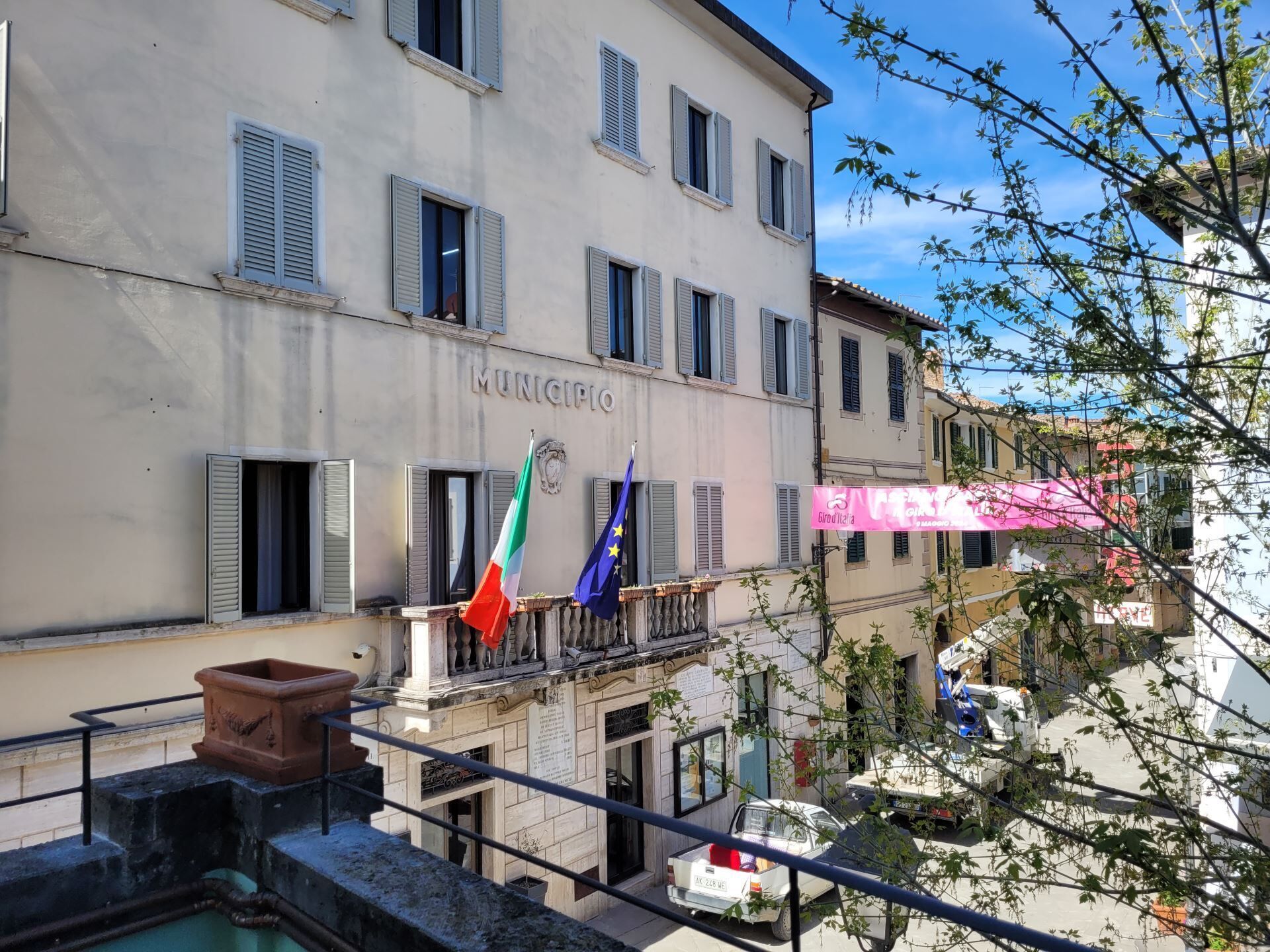 A building with 'MUNICIPIO' signage, Italian and EU flags, and a pink awning.