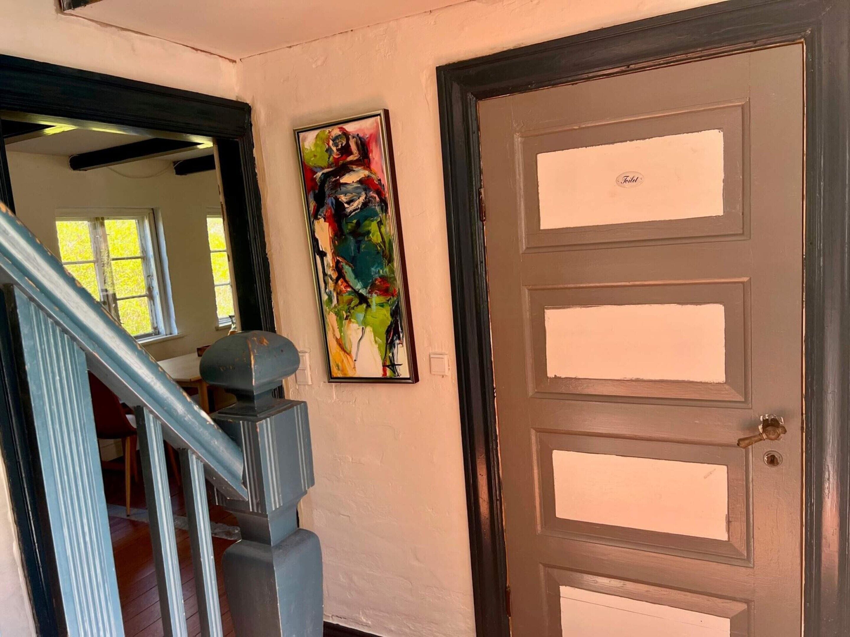A staircase with a handrail, a door with a brass handle, and a colorful abstract painting on the wall.