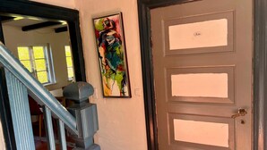 Una escalera con barandilla, una puerta con picaporte de latón y un cuadro abstracto de colores en la pared.