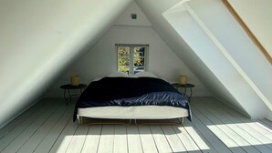 Un dormitorio con techo inclinado, una cama, dos mesitas de noche y una ventana.