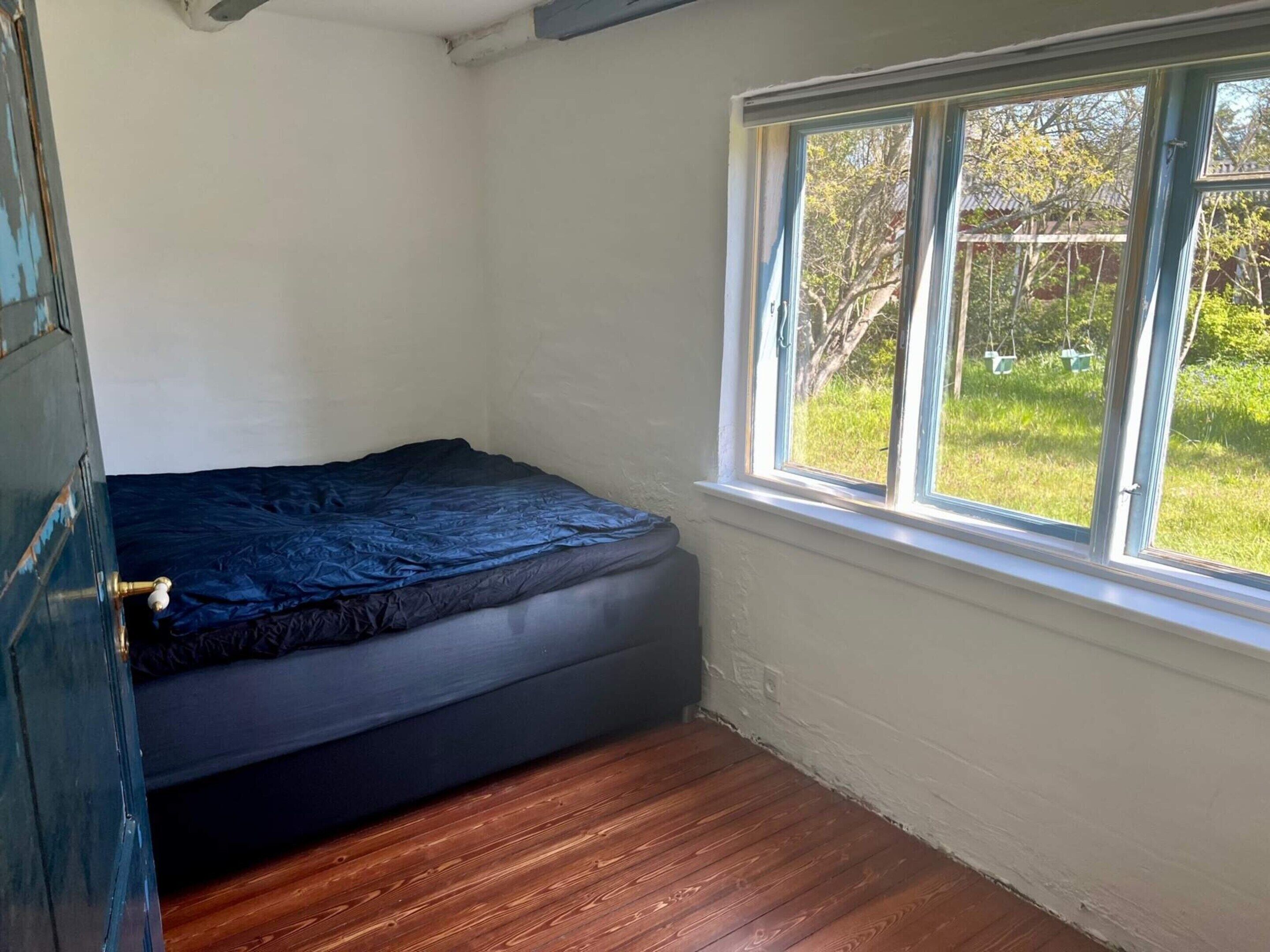 Una stanza piccola con un letto singolo, una finestra e una porta.