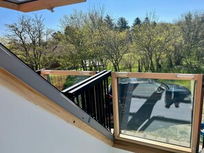 A balcony with a glass door and wooden railing, overlooking a residential area with trees and a parked car. - 6 Person Holiday Home in Skagen (Skagen)