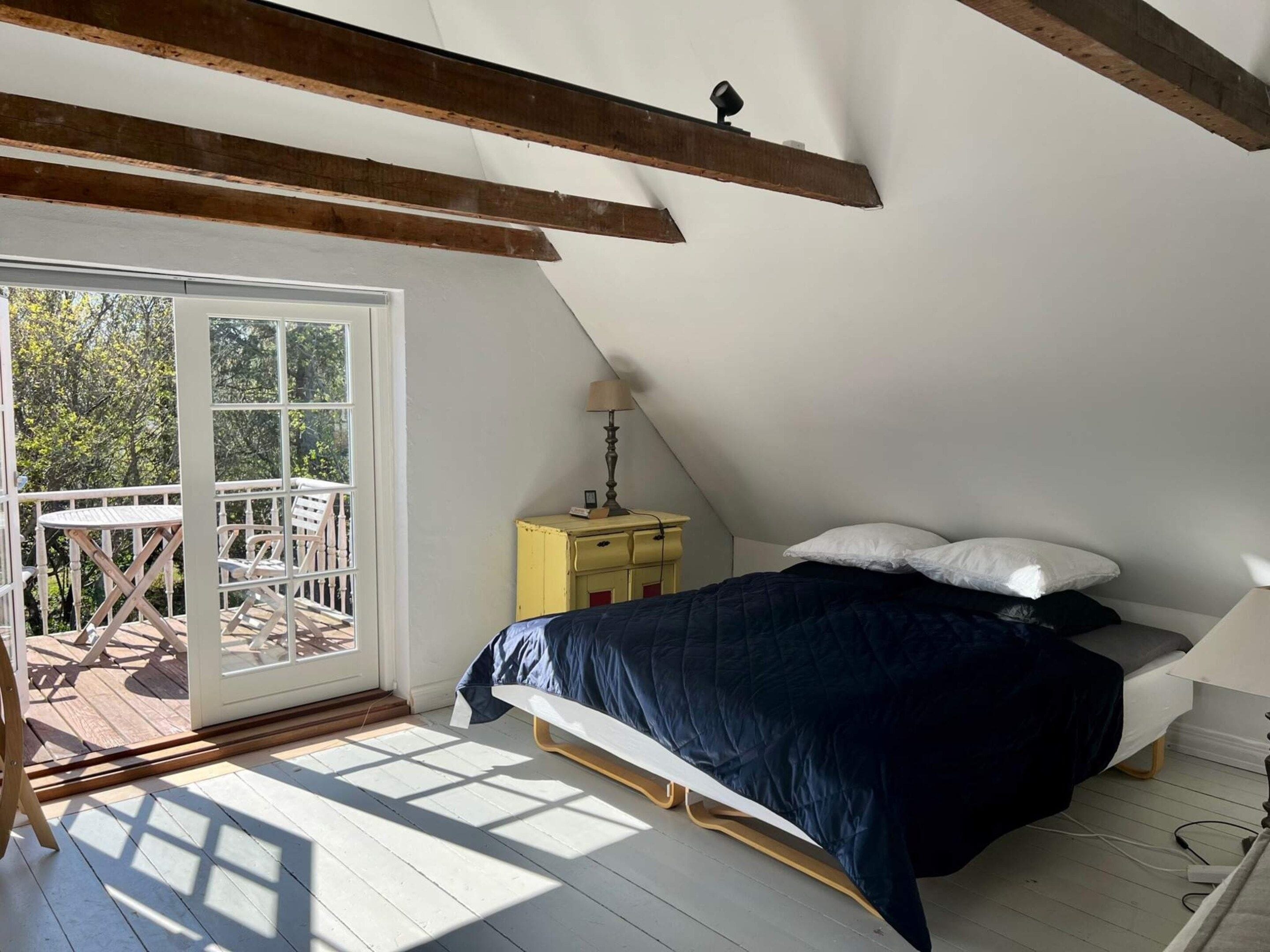 A bedroom with a bed, a nightstand, a lamp, and a view of the outdoors through a sliding door.