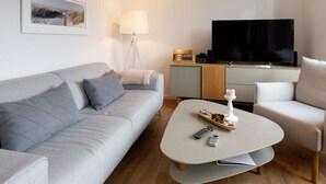 A modern living room with a grey sofa, a white coffee table, and a TV on a wooden cabinet. - Holiday Home Traumstuuv (Varel)