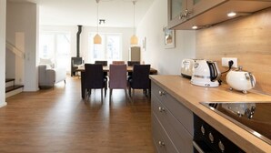 A modern kitchen with wooden cabinets, a built-in oven, and a dining area with a table and chairs. - Holiday Home Traumstuuv (Varel)