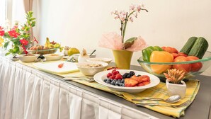 Un bufé de desayuno con diversas frutas, verduras y un jarrón con flores.