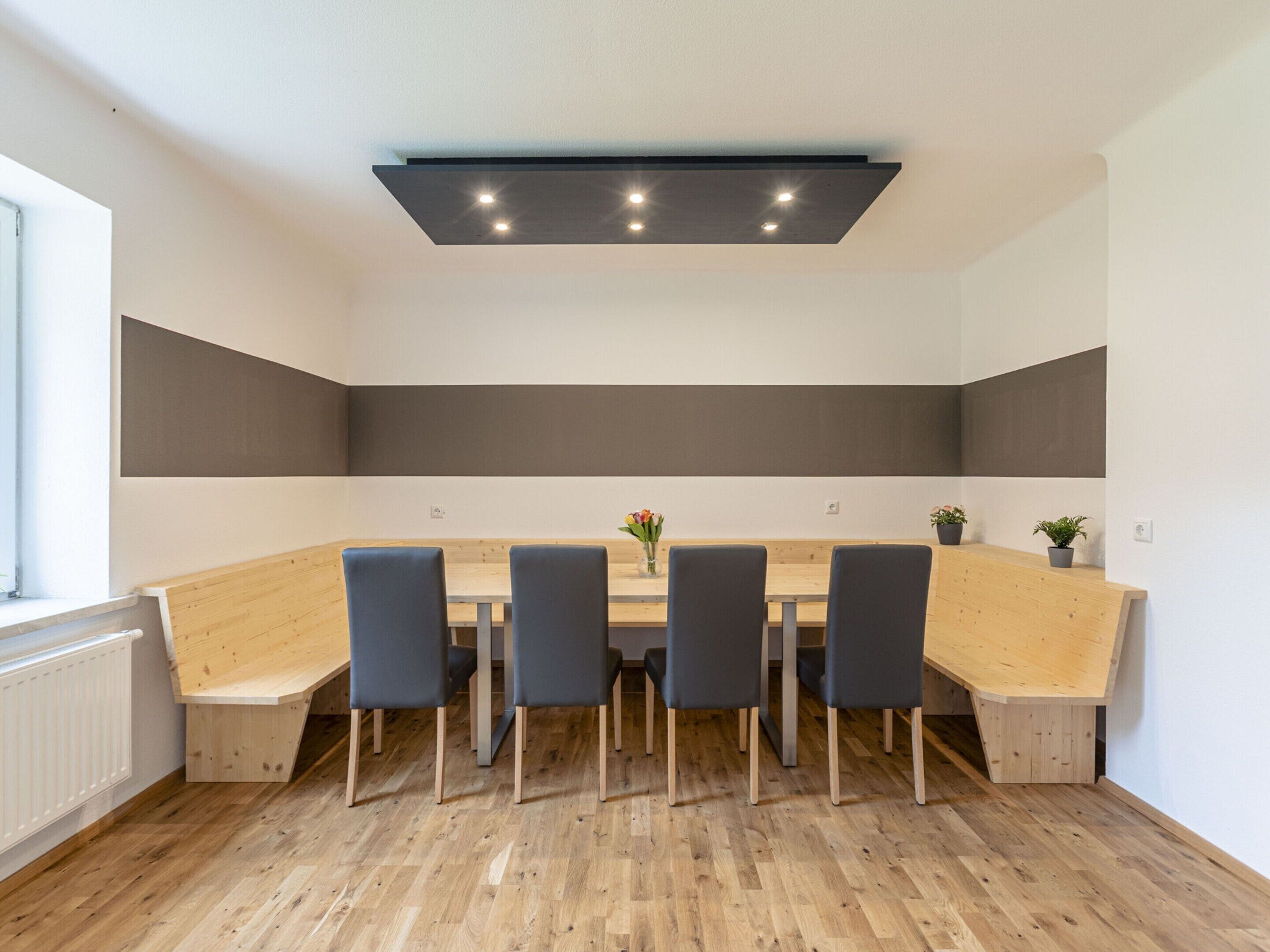 A modern dining area with a long wooden table, six chairs, and a ceiling light fixture.